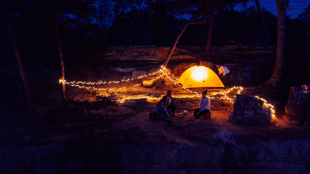 A cozy campsite illuminated by string lights and a glowing tent illuminated under a night sky with the best tent lantern.